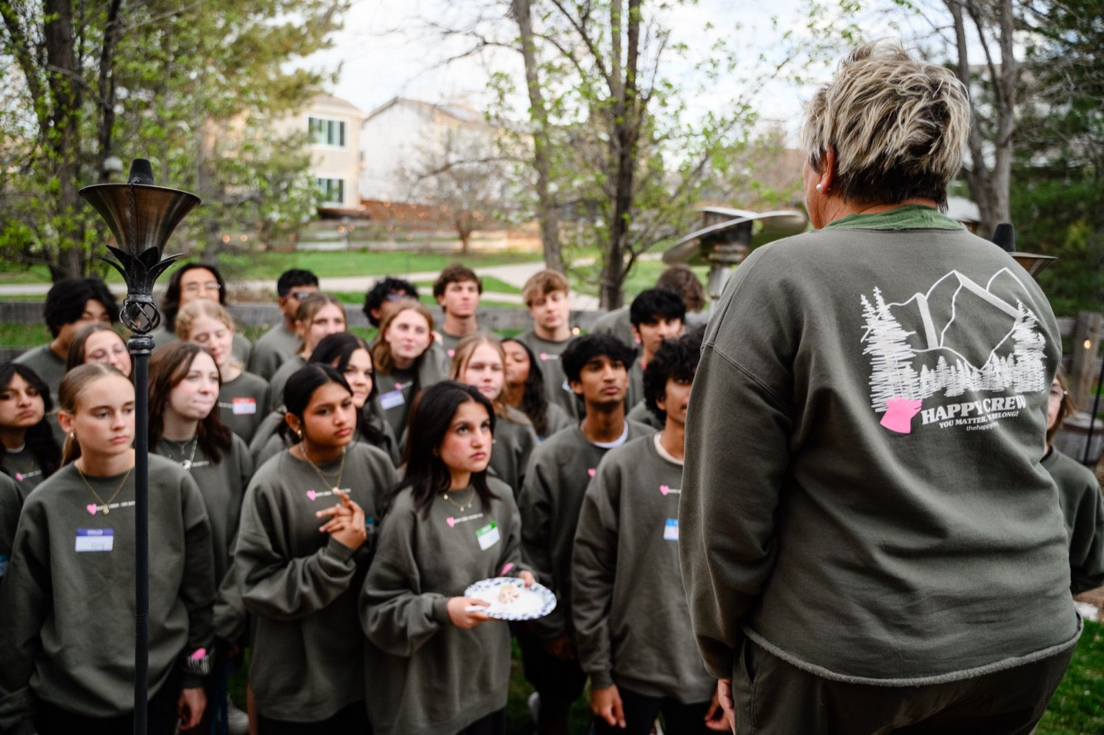 Student leaders in matching Happy Crew sweatshirts, listening to Amy outside