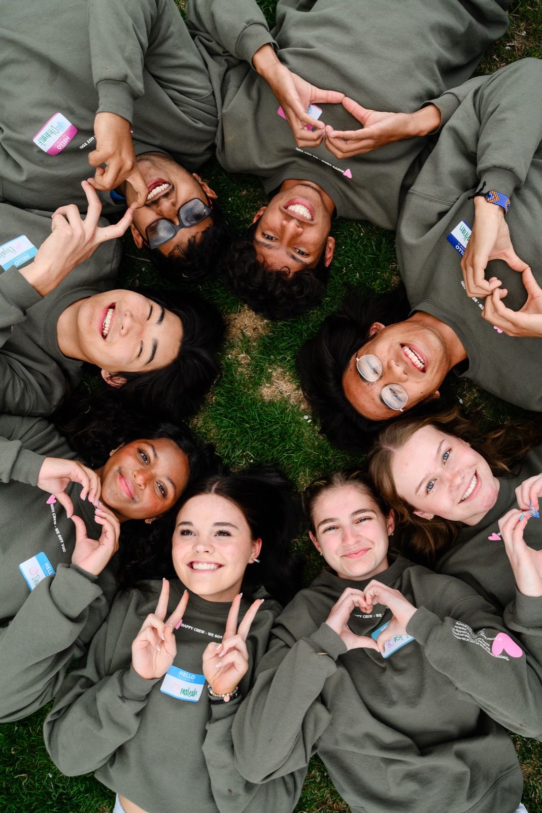 Teens lying in a circle on the grass, heads together, making hearts with their hands