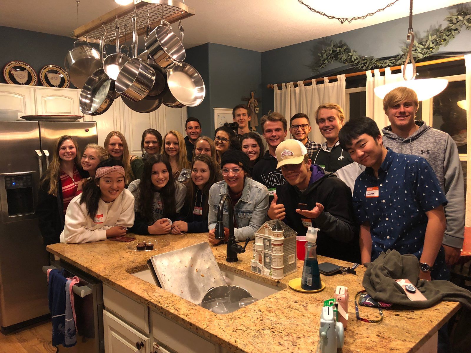 A kitchen packed with teens in name tags, crowded around the island, smiling