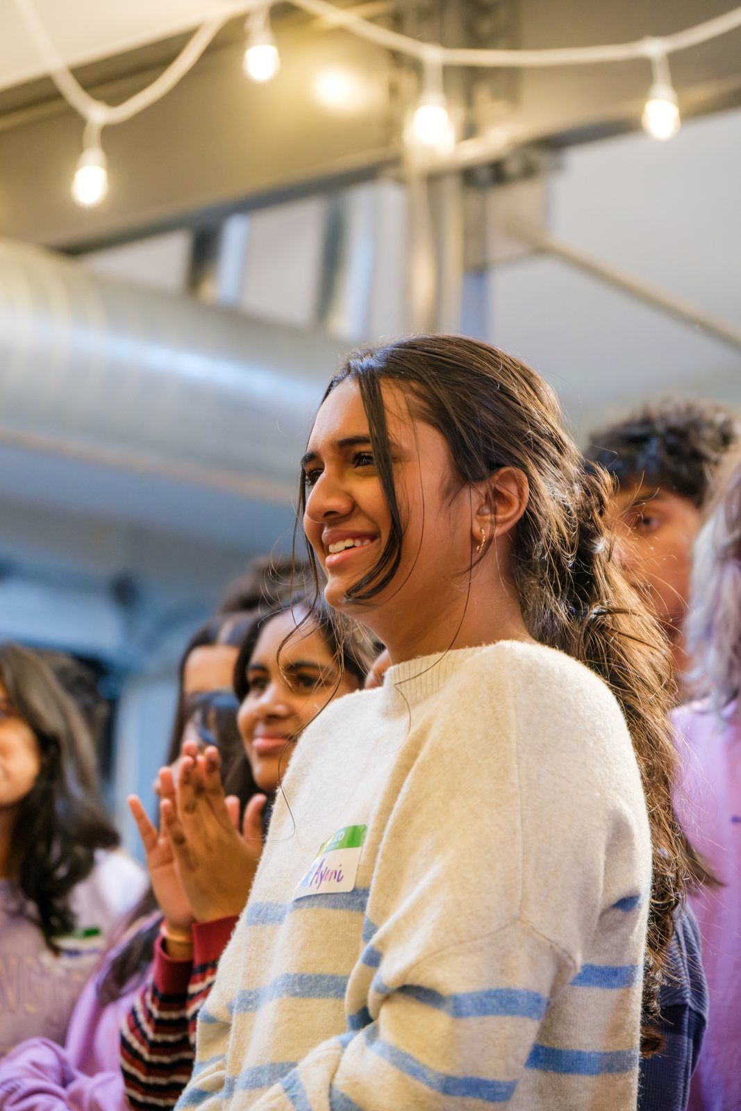 A teen laughing and clapping under the string lights