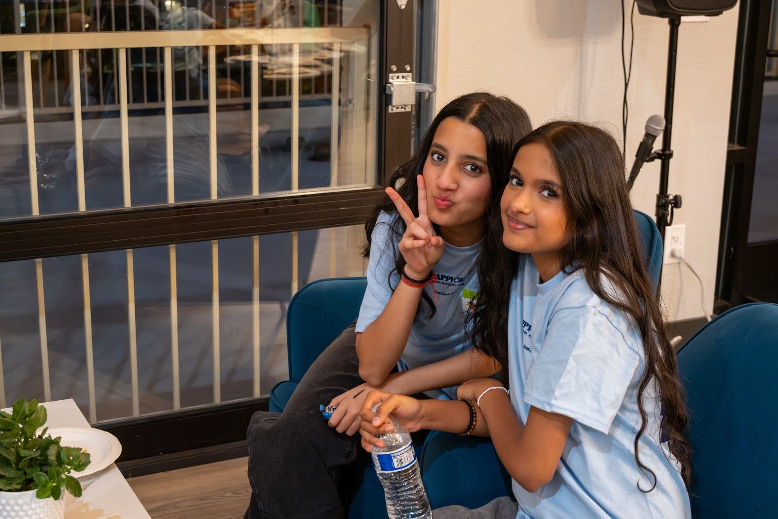 Two teens on a couch upstairs, smiling, one making a peace sign